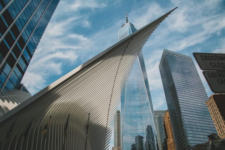 cheap hotels nyc, Dramatic angle of New York City's One World Trade Center and surrounding skyscrapers against a blue sky.