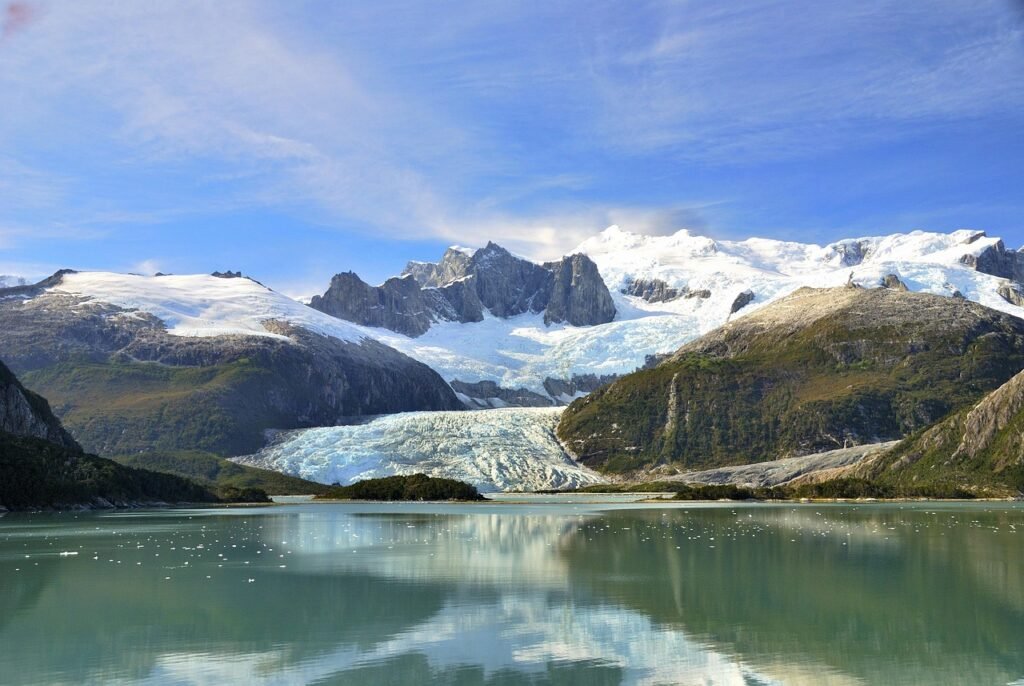 A panoramic ultra-realistic photo of a picturesque Patagonian summer landscape. In the foreground, a vibrant green meadow filled with blooming wildflowers. A crystal-clear lake reflects the towering Andes mountains in the middle ground, their snow-capped peaks glistening under the warm sun. In the background, rugged cliffs and glaciers stretch out as far as the eye can see. A flock of Magellanic penguins waddles along the shore, basking in the long daylight hours. Soft, diffused lighting illuminates the scene, creating a serene and awe-inspiring atmosphere. photo of a picturesque Patagonian summer landscape. In the foreground, a vibrant green meadow filled with blooming wildflowers. A crystal-clear lake reflects the towering Andes mountains in the middle ground, their snow-capped peaks glistening under the warm sun. In the background, rugged cliffs and glaciers stretch out as far as the eye can see. A flock of Magellanic penguins waddles along the shore, basking in the long daylight hours. Soft, diffused lighting illuminates the scene, creating a serene and awe-inspiring atmosphere.