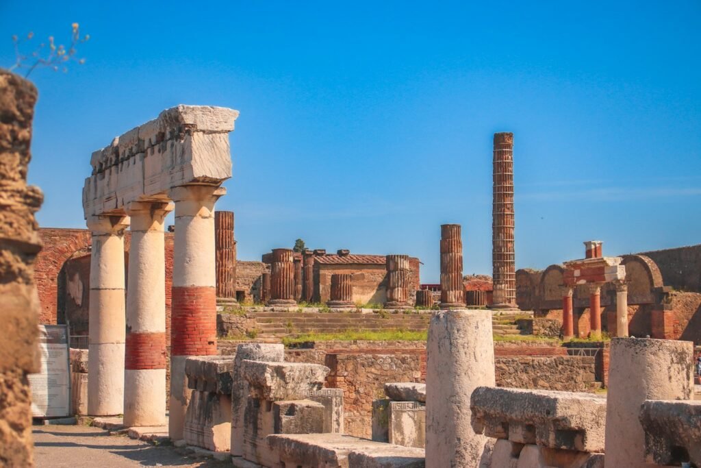 A breathtaking panoramic view of the iconic landscapes of southern Italy. In the foreground, the ancient ruins of Pompeii stand in the shadow of the mighty Mount Vesuvius, its snow-capped peak rising majestically into the azure sky. In the middle ground, the winding roads of the Amalfi Coast hug the rugged coastline, dotted with charming seaside villages and picturesque harbors. In the background, the turquoise waters of the Tyrrhenian Sea stretch out to the horizon, with the striking silhouettes of the Sorrentine Peninsula and the island of Capri visible in the distance. The scene is bathed in warm, golden sunlight, creating a sense of timeless beauty and tranquility. A breathtaking panoramic view of the iconic landscapes of southern Italy. In the foreground, the ancient ruins of Pompeii stand in the shadow of the mighty Mount Vesuvius, its snow-capped peak rising majestically into the azure sky. In the middle ground, the winding roads of the Amalfi Coast hug the rugged coastline, dotted with charming seaside villages and picturesque harbors. In the background, the turquoise waters of the Tyrrhenian Sea stretch out to the horizon, with the striking silhouettes of the Sorrentine Peninsula and the island of Capri visible in the distance. The scene is bathed in warm, golden sunlight, creating a sense of timeless beauty and tranquility ,the ruins of the ancient city of pompei