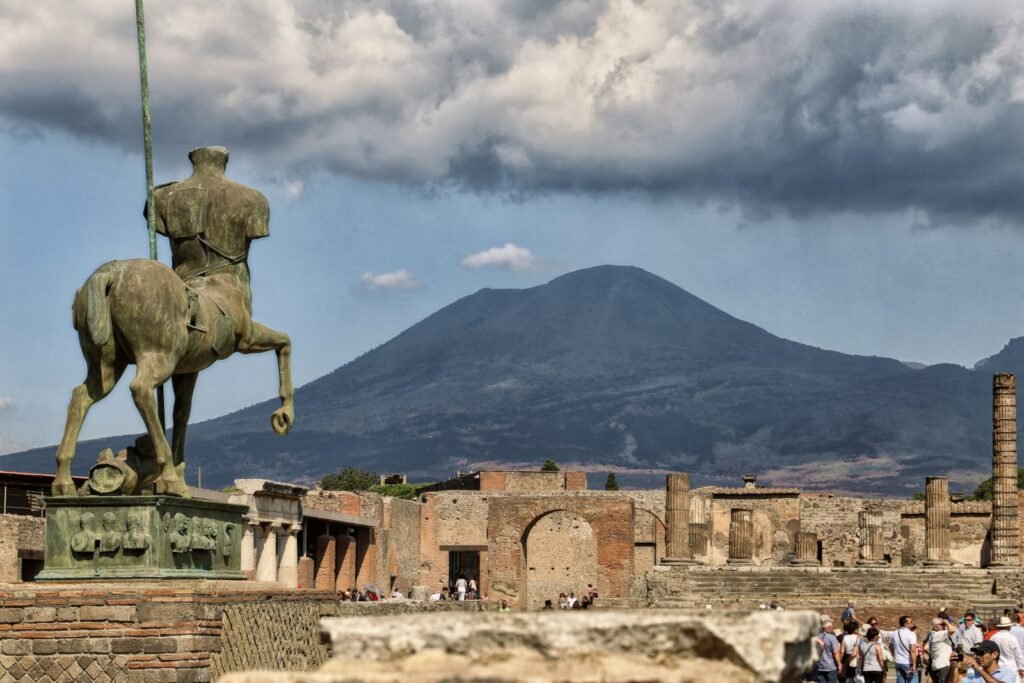 A meticulously composed photograph capturing the grandeur of Pompeii, showcasing a small group of visitors exploring the ancient ruins. The foreground features a family of four, casually strolling through the well-preserved streets, their expressions reflecting a sense of wonder and awe. The middle ground showcases the iconic architecture, with intricate details of the ancient buildings and monuments. The background is a panoramic view of the Vesuvius volcano, its majestic presence looming over the historic site. The lighting is warm and natural, casting a golden glow across the scene, creating a sense of timelessness and tranquility. The overall composition is carefully balanced, capturing the essence of a private, family-friendly Pompeii day tour in a visually captivating manner. A meticulously composed photograph capturing the grandeur of Pompeii, showcasing a small group of visitors exploring the ancient ruins. The foreground features a family of four, casually strolling through the well-preserved streets, their expressions reflecting a sense of wonder and awe. The middle ground showcases the iconic architecture, with intricate details of the ancient buildings and monuments. The background is a panoramic view of the Vesuvius volcano, its majestic presence looming over the historic site. The lighting is warm and natural, casting a golden glow across the scene, creating a sense of timelessness and tranquility. The overall composition is carefully balanced, capturing the essence of a private, family-friendly Pompeii day tour in a visually captivating manner,people on historical place