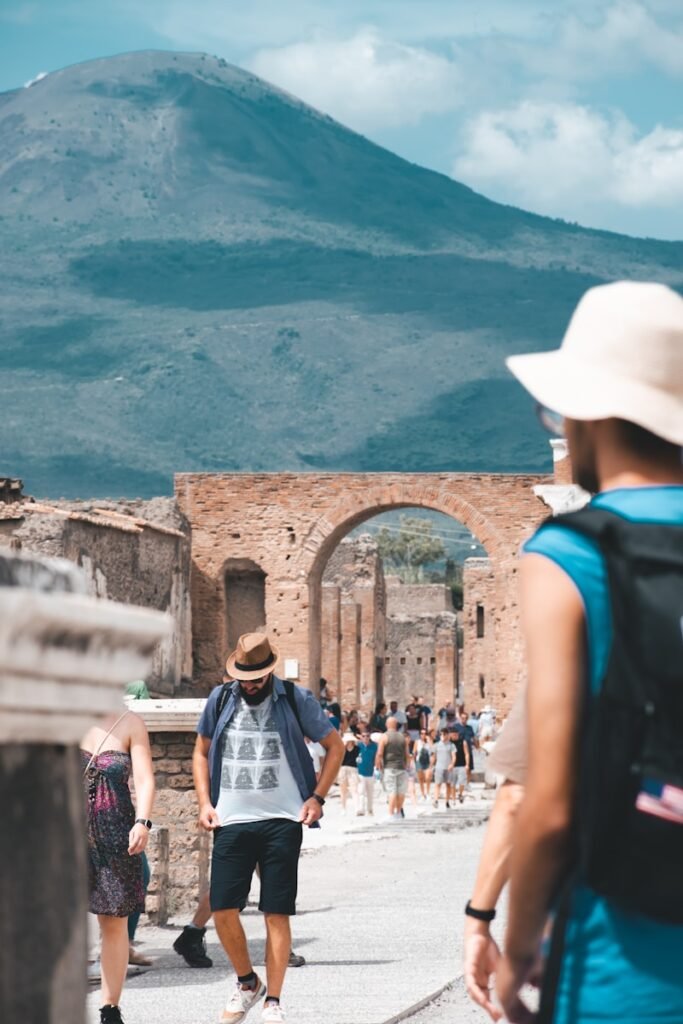 A group of travelers standing in the ancient ruins of Pompeii, gazing in awe at the preserved structures and artifacts around them. The foreground features a tour guide gesturing animatedly, captivating the group's attention with their passionate narration. The middle ground showcases the iconic Mount Vesuvius in the distance, its snow-capped peak casting a serene, dramatic backdrop. Warm, golden sunlight filters through the columns and archways, creating a sense of timelessness and wonder. The overall atmosphere conveys the immersive, unforgettable experience of exploring this UNESCO World Heritage Site with the guidance of a knowledgeable, engaging local expert. A group of travelers standing in the ancient ruins of Pompeii, gazing in awe at the preserved structures and artifacts around them. The foreground features a tour guide gesturing animatedly, captivating the group's attention with their passionate narration. The middle ground showcases the iconic Mount Vesuvius in the distance, its snow-capped peak casting a serene, dramatic backdrop. Warm, golden sunlight filters through the columns and archways, creating a sense of timelessness and wonder. The overall atmosphere conveys the immersive, unforgettable experience of exploring this UNESCO World Heritage Site with the guidance of a knowledgeable, engaging local expert.
