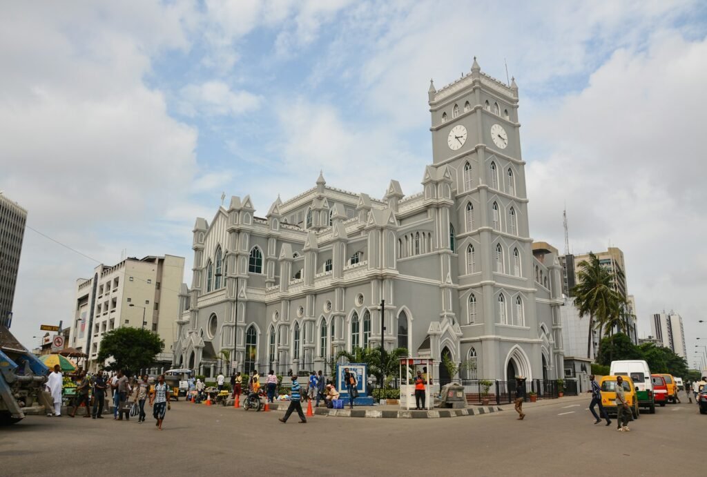 A vibrant, sun-drenched scene of Sri Lanka's budget travel experiences. In the foreground, a large white building with a clock tower, a local street market bustles with colorful spices, fresh produce, and artisanal crafts. Smiling vendors beckon passersby to explore their wares. In the middle ground, a group of backpackers navigate the maze of narrow alleyways, their faces alight with wonder. Towering in the background, the iconic silhouette of Sigiriya Rock juts into a cloudless azure sky, casting a serene, timeless presence over the lively proceedings. The overall atmosphere is one of energy, authenticity, and the sense of discovery that makes Sri Lanka such an enticing destination for the budget-conscious traveler.