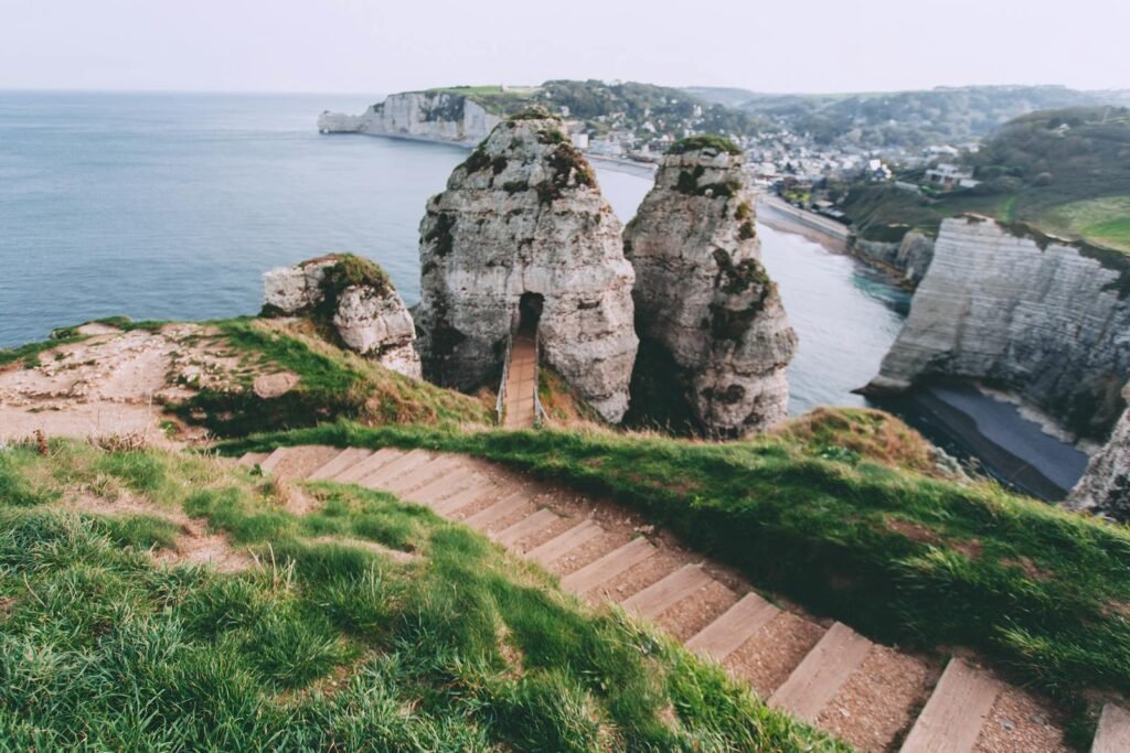 A sweeping panorama of the Normandy coast, with its iconic chalk cliffs and picturesque seaside towns. In the foreground, the ruins of German fortifications stand as solemn reminders of the D-Day landings, their weathered bunkers and gun emplacements casting long shadows across the sands. In the middle ground, narrow country roads wind through verdant farmland, dotted with quaint villages and church spires. The distant horizon is dominated by the rolling hills of northern France, their slopes blanketed in lush vegetation. Warm, golden light bathes the scene, evoking the sense of a bygone era. This comprehensive landscape captures the essence of Normandy's crucial role in World War II, a destination ripe for immersive historical exploration.