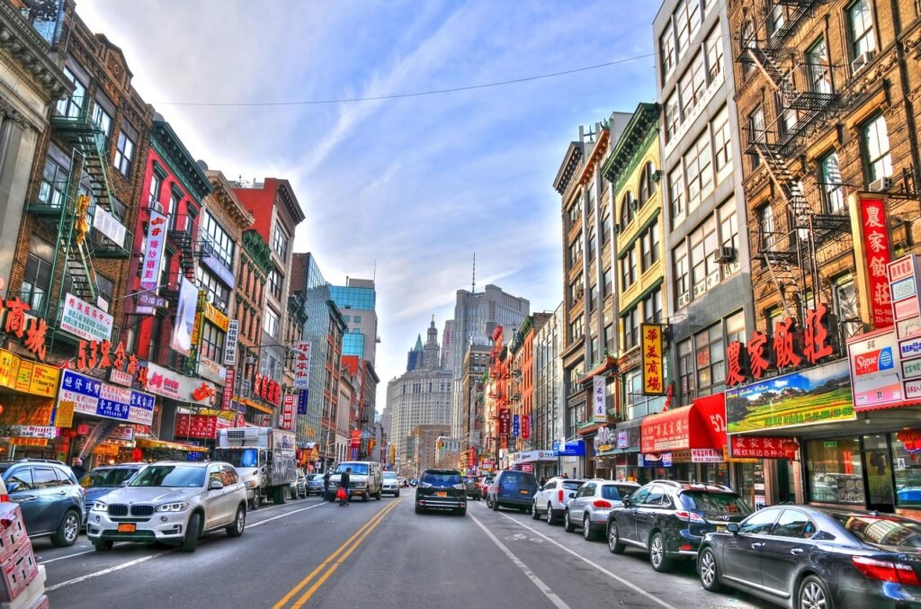 A bustling Chinatown street, lined with vibrant neon signs and busy storefronts. In the foreground, an array of traditional Chinese grocery essentials - bamboo steamers, soy sauce bottles, and fragrant spices. At the center, a group of locals huddle around a renowned soup dumpling vendor, their faces illuminated by the warm glow of the steam as they savor the juicy, savory morsels. In the background, the towering skyscrapers of New York City loom, creating a striking contrast between old and new. The scene is captured in an ultra-realistic, high-resolution photograph, conveying the energy, flavor, and cultural vibrancy of this iconic Chinatown neighborhood. A bustling Chinatown street, lined with vibrant neon signs and busy storefronts. In the foreground, an array of traditional Chinese grocery essentials - bamboo steamers, soy sauce bottles, and fragrant spices. At the center, a group of locals huddle around a renowned soup dumpling vendor, their faces illuminated by the warm glow of the steam as they savor the juicy, savory morsels. In the background, the towering skyscrapers of New York City loom, creating a striking contrast between old and new. The scene is captured in an ultra-realistic, high-resolution photograph, conveying the energy, flavor, and cultural vibrancy of this iconic Chinatown neighborhood.