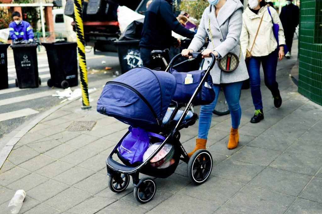 A bustling urban scene in New York City, capturing the lively energy of parents navigating the city with their young children. In the foreground, a diverse group of families push strollers along the crowded sidewalk, dodging pedestrians and weaving through the flow of foot traffic. In the middle ground, a subway station entrance stands as a gateway to the city's efficient transportation system, where parents carry sleeping toddlers onto waiting trains. The background showcases the iconic skyscrapers and landmarks of the Manhattan skyline, bathed in warm, golden afternoon light. The overall atmosphere conveys the challenges and joys of exploring the Big Apple with little ones in tow.