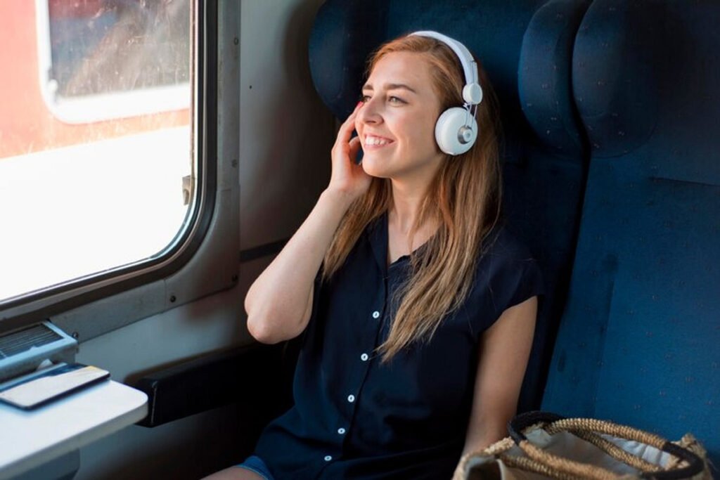 A woman traveling with a white noise canceling headphones on while smiling.