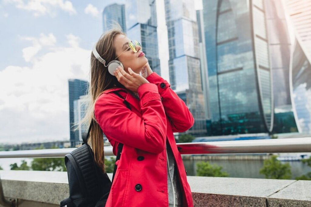 A woman in red traveling in the city with a noise canceling headphones on, listening to music.