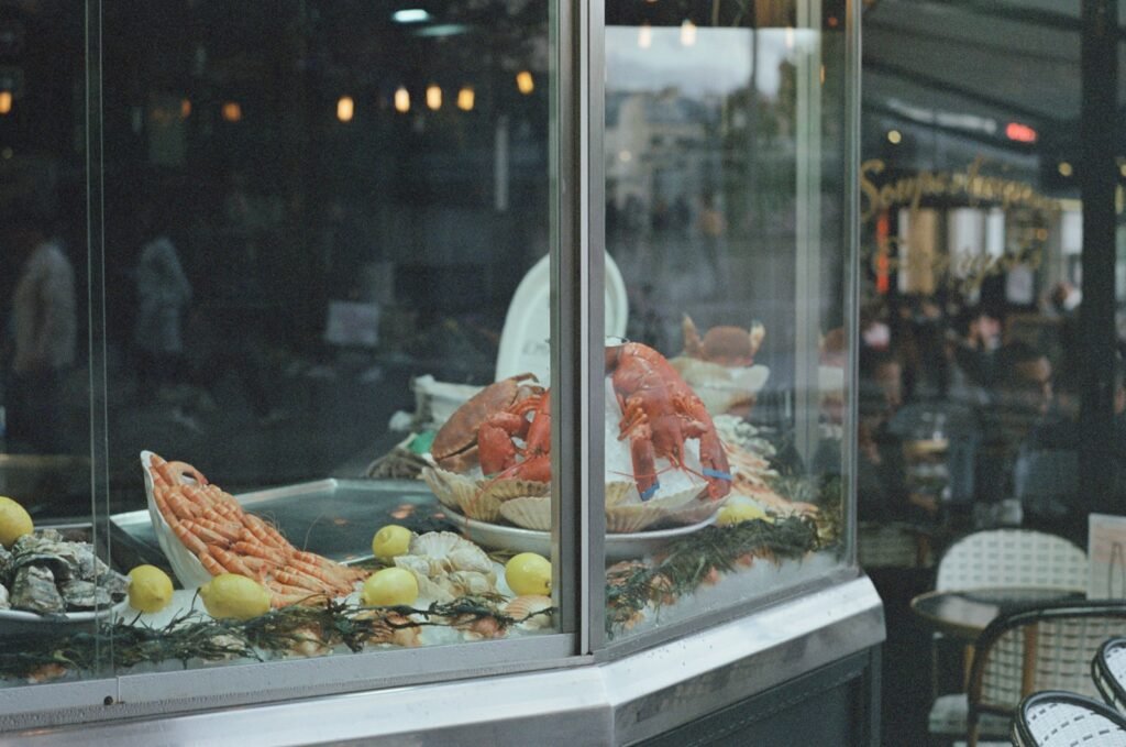 A bustling cityscape in New York's upscale restaurant district, bathed in warm, golden evening light. In the foreground, the grand facade of a renowned seafood institution, its elegant signage and ornate architectural details commanding attention. Patrons dine al fresco at white-linen-clad tables, savoring the fresh catch of the day. In the middle ground, a row of high-end eateries, each with its own distinctive style and allure, beckoning discerning diners. The background is a tapestry of skyscrapers and twinkling city lights, setting the stage for an unforgettable dining experience. The scene exudes a sense of sophistication, indulgence, and the culinary heritage that has made New York a global gastronomic capital. A display case with lobsters and other seafood in it, New York's upscale restaurant district, bathed in warm, golden evening light. In the foreground, the grand facade of a renowned seafood institution, its elegant signage and ornate architectural details commanding attention. Patrons dine al fresco at white-linen-clad tables, savoring the fresh catch of the day. In the middle ground, a row of high-end eateries, each with its own distinctive style and allure, beckoning discerning diners. The background is a tapestry of skyscrapers and twinkling city lights, setting the stage for an unforgettable dining experience. The scene exudes a sense of sophistication, indulgence, and the culinary heritage that has made New York a global gastronomic capital.