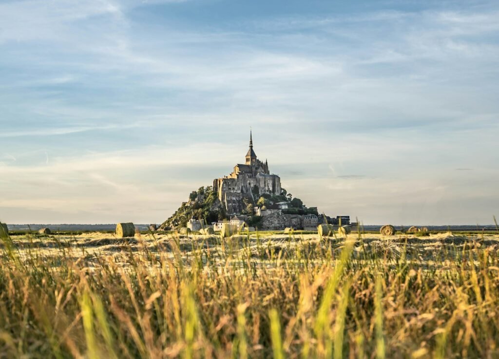 Sweeping landscape of Normandy's rugged coastline, dotted with crumbling bunkers and memorials to the fallen. In the middle ground, a cobblestone village nestled amidst rolling hills and verdant forests. Warm afternoon light bathes the scene, casting long shadows. As the viewer's gaze travels inland, the landscape transforms - dense, ancient forests give way to the war-scarred ruins of Nuremberg. Rubble-strewn streets, shattered buildings, and the imposing silhouette of a grand, damaged castle loom in the distance, shrouded in an ominous haze. The atmosphere is one of quiet reverence, a haunting reminder of the profound tragedies and resilience of the past.