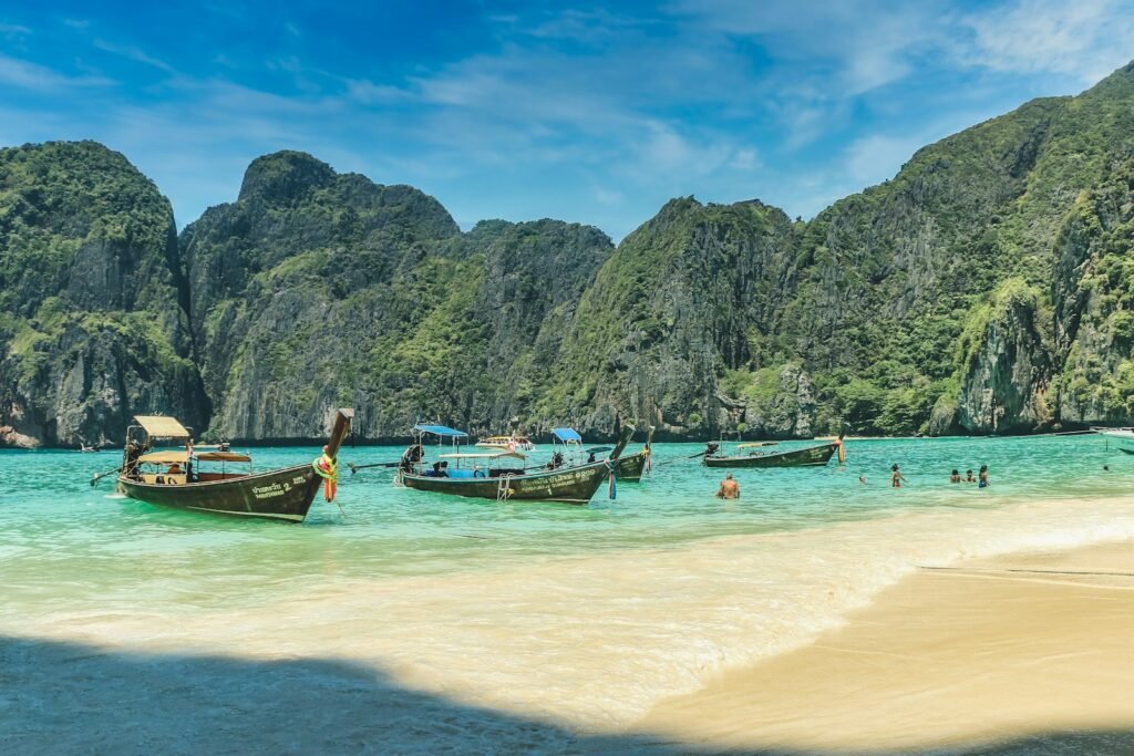 A tropical paradise in Thailand unfolds, where pristine beaches kiss crystal-blue waters and swaying palm trees cast gentle shadows. In the foreground, sun-kissed beachgoers lounge on plush, white sand, their laughter and carefree spirits capturing the essence of a perfect escape. The middle ground reveals a vibrant coastal town, its colorful buildings and bustling marketplace a testament to the region's rich cultural heritage. Beyond, rugged limestone cliffs rise majestically, their jagged profiles silhouetted against a breathtaking sunset sky. Warm, golden light bathes the entire scene, creating a sense of tranquility and natural beauty that is quintessentially Thai.