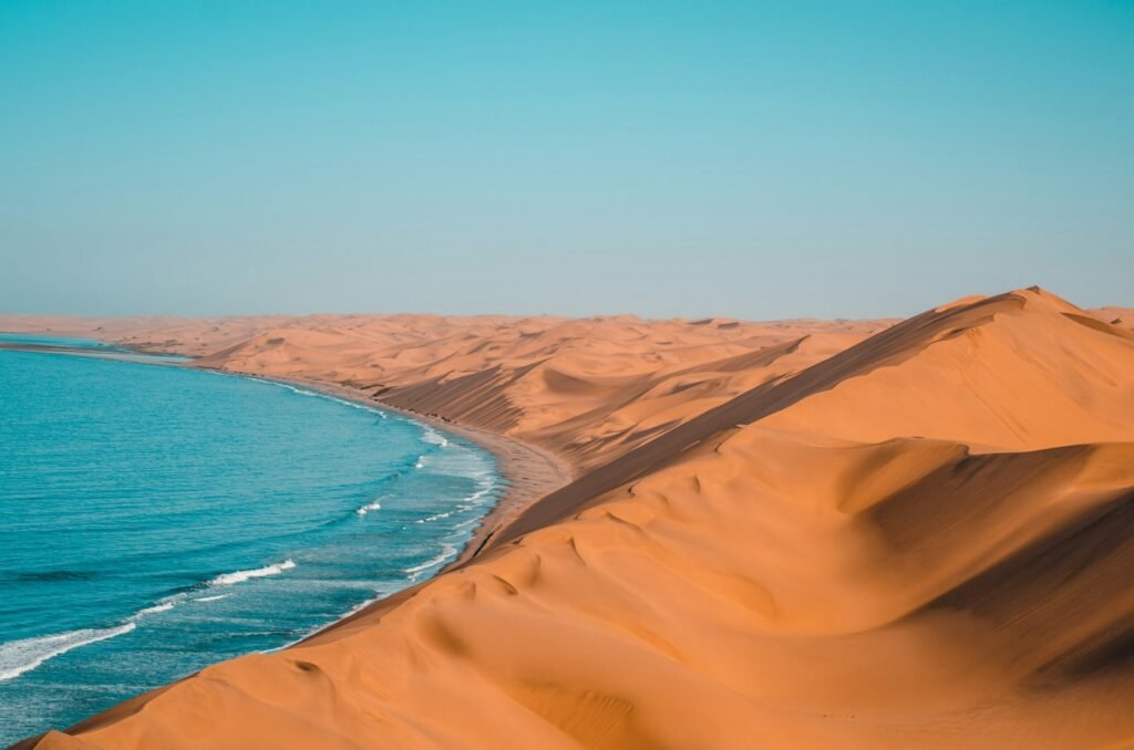 A breathtaking photo of the Arabian Peninsula's captivating landscapes. In the foreground, rugged mountains and windswept dunes stretch out, their warm hues casting a golden glow. Winding through the center, a serene wadi (dry riverbed) with shimmering pools and lush vegetation. Beyond, the shimmering azure waters of the Gulf of Oman meet the horizon, dotted with traditional dhow boats. The sky is filled with wispy clouds, creating dramatic shadows and highlights that accentuate the region's dramatic topography. The scene exudes a sense of timeless tranquility, capturing the essence of Oman's enchanting desert, coastal, and cultural wonders.