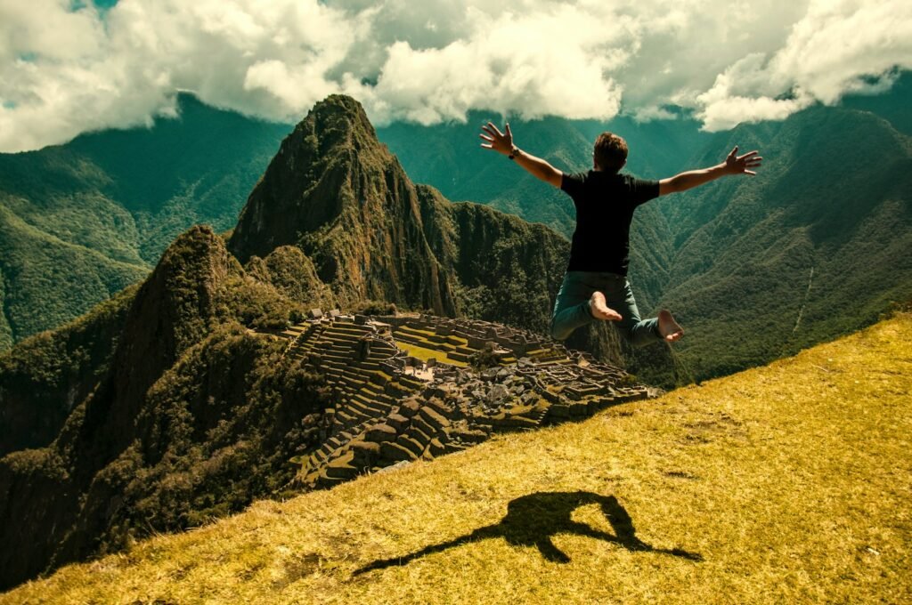 A panoramic vista of the iconic Machu Picchu ruins, in the sunny afternoon. A lone hiker jumps atop the Inca Trail, gazing out over the lush, terraced landscape. Sunlight filters through the cloud cover, casting a warm, golden glow on the ancient stone structures. The path winds gracefully through the mountainous terrain, offering breathtaking views at every turn. The scene conveys a sense of tranquility and adventure, perfectly capturing the essence of the best time to hike this legendary Incan citadel.